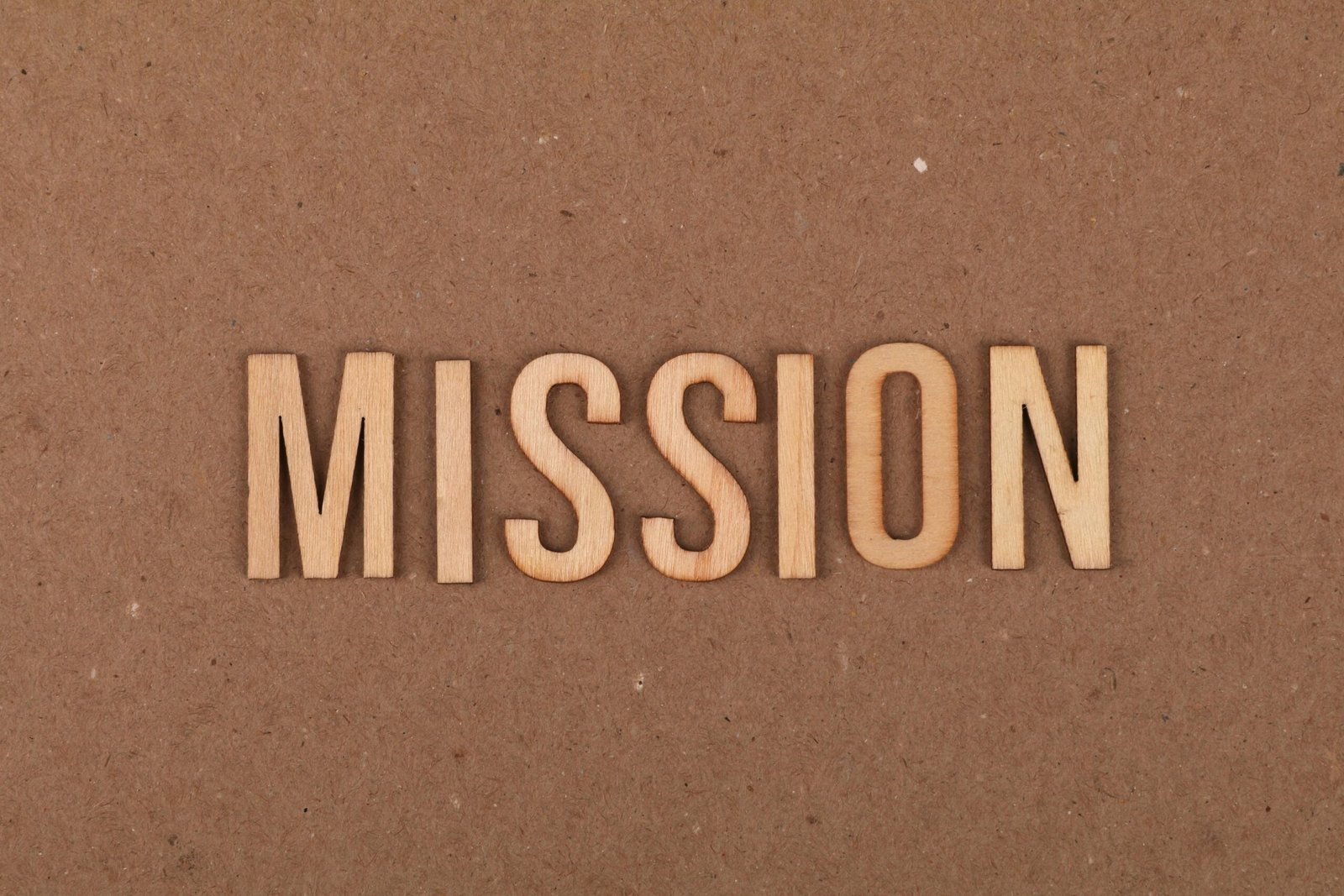 Wooden letters spelling 'MISSION' on textured cardboard background, emphasizing goals and purpose.